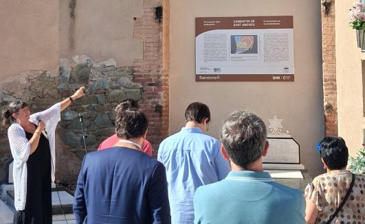 Noemí Cortès, presidenta de la IBEC, assenyala el plafó commemoratiu del recinte protestant del Cementiri de Sant Andreu